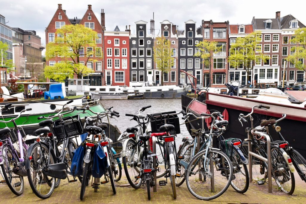 Row of bicycles lined up in front of canal in Amsterdam with row of multicoloured Dutch houses on the other side of the water