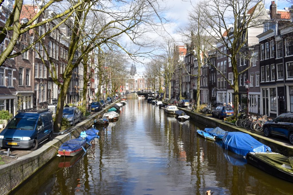Looking down a canal in Amsterdam with Dutch houses either side and boats moored on banks of canal