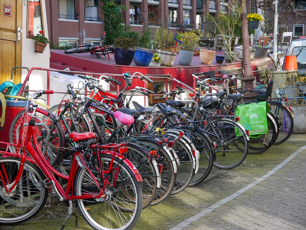 Row of bicycles by river and houseboats. Red bike in the foreground