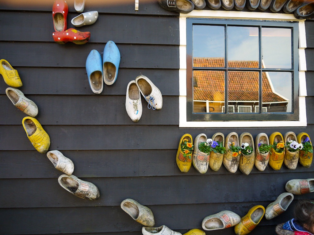 The side wall of a wooden house painted black with a window and multicoloured painted clogs decorating the side of building