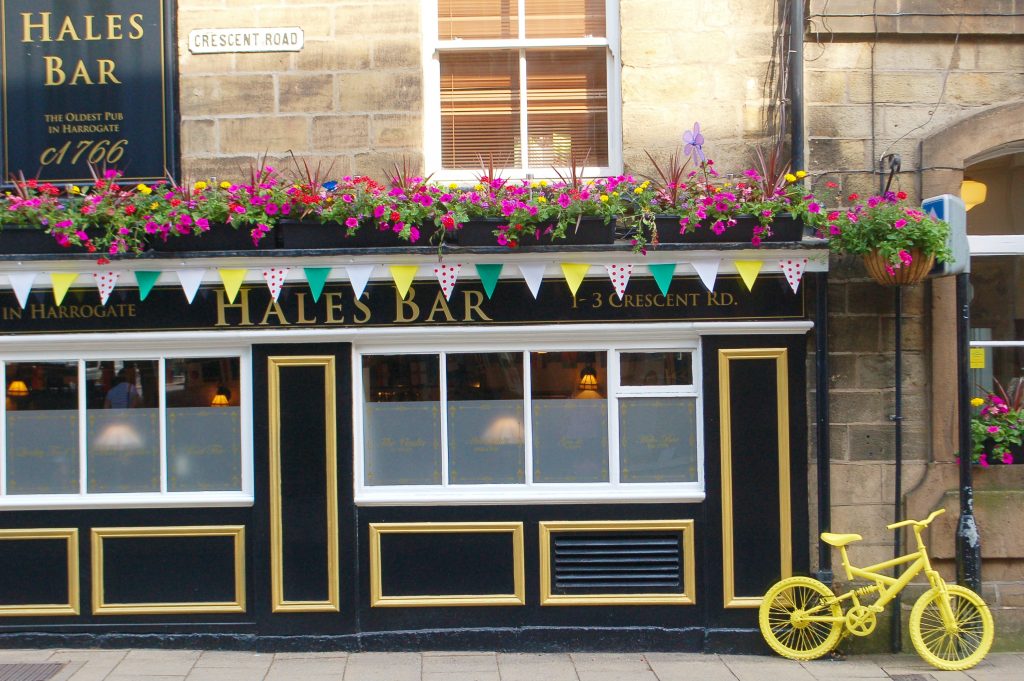 Photo of the front of a pub painted black with white woodwork. It has bunting and flowers over the windows and a yellow bike to the right hand side