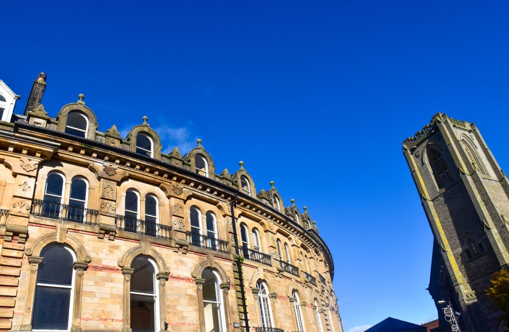 Landscape shot of a curved Victorian building to the left of the photo (3 storeys high) and a church steeple to the right hand side. Shot taken upwards towards a blue sky